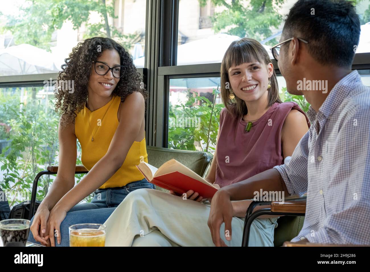 De jeunes étudiants d'université heureux d'avoir un moment de détente dans une cafétéria.Groupe de personnes multiraciales parlant, s'amusant et lisant un livre Banque D'Images