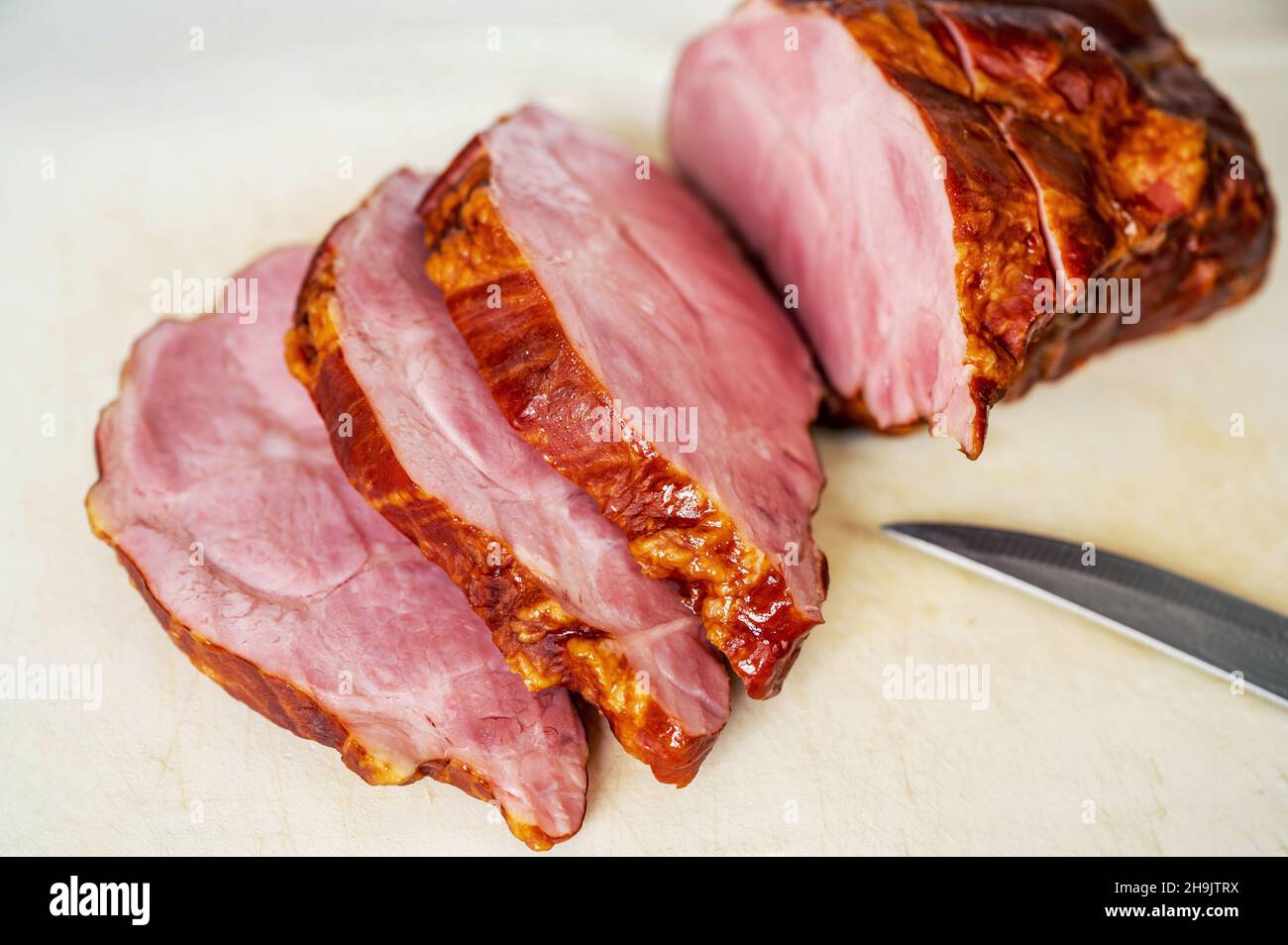 Tranché de viande fumée sur une planche de cuisine blanche avec couteau, gros plan. Banque D'Images