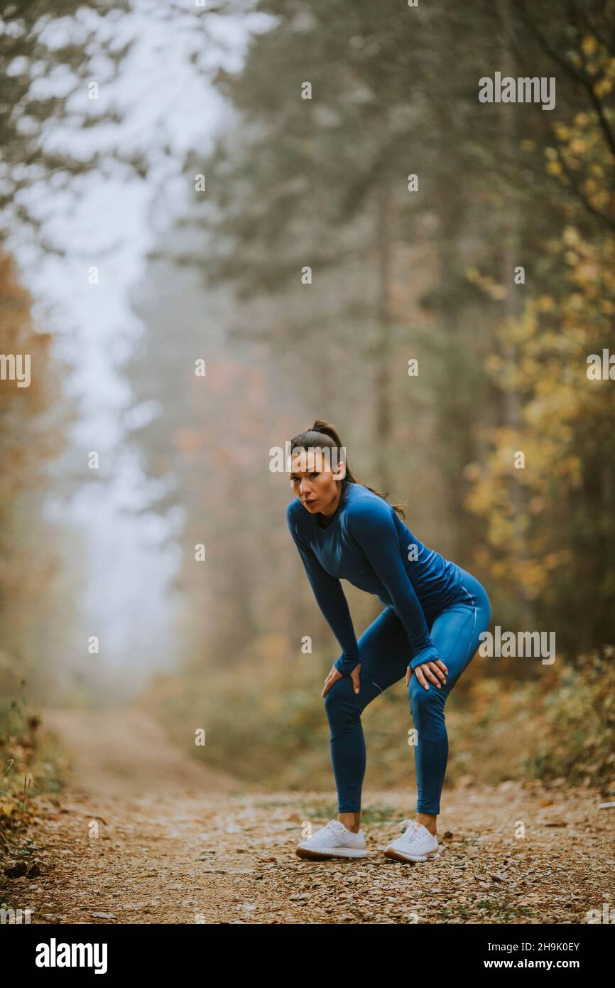 Une jolie jeune femme fait une pause lors d'un exercice en plein air sur le sentier forestier à l'automne Banque D'Images