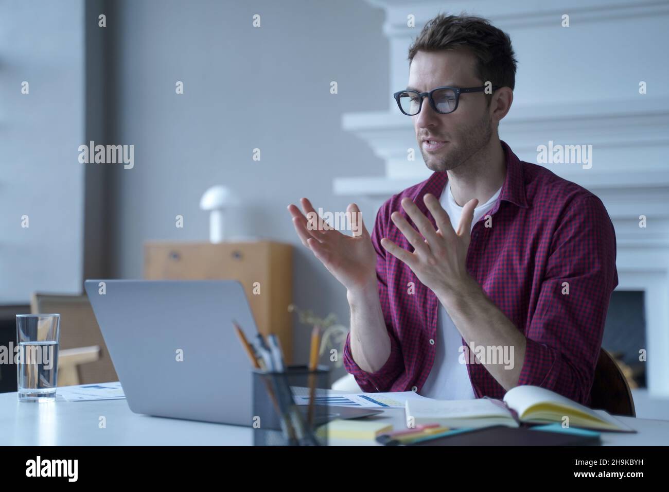 Jeune homme allemand concentré en lunettes et vêtements décontractés participant à la réunion virtuelle en ligne Banque D'Images