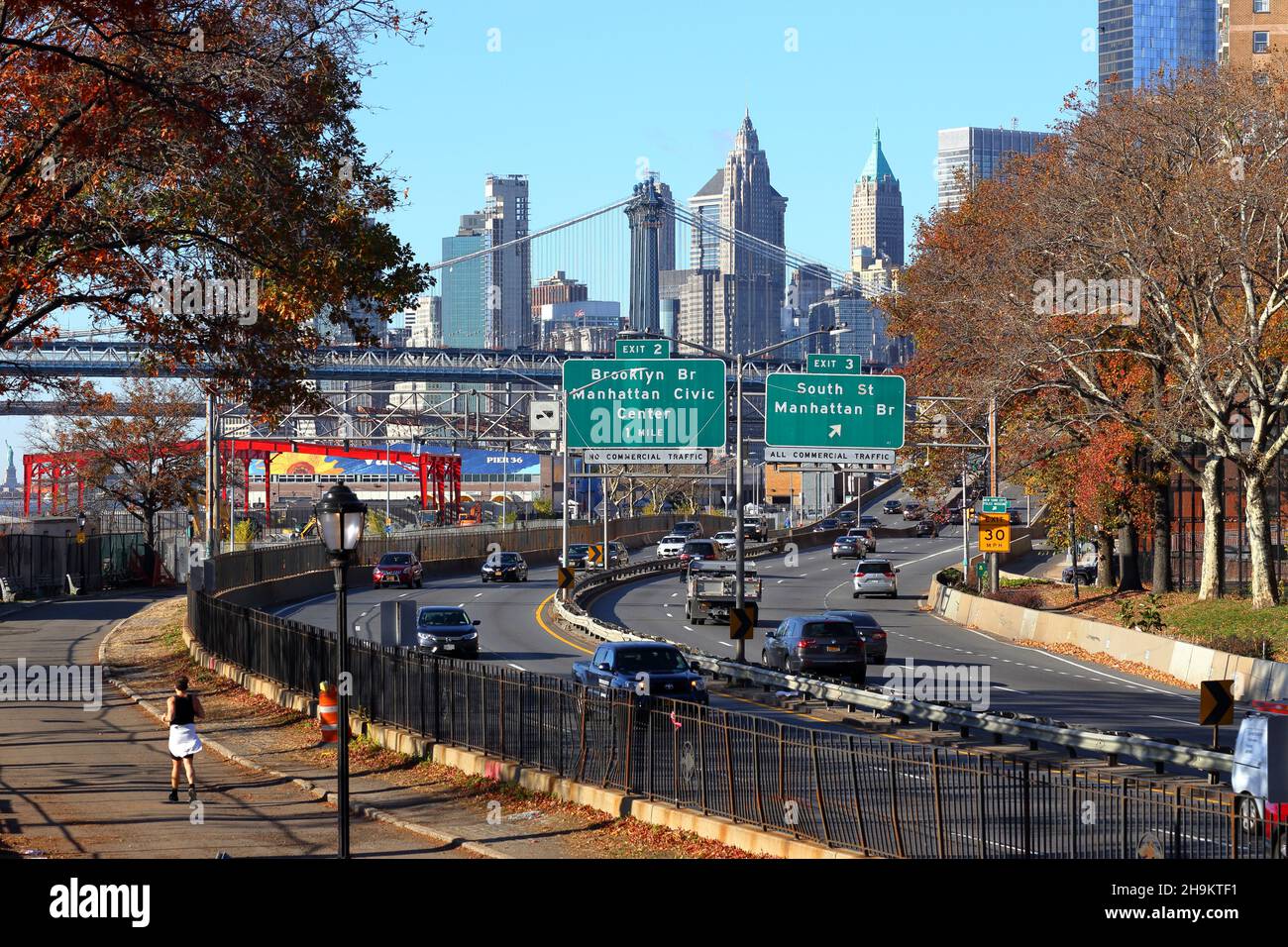 Un jogging sur l'East River Greenway le long de FDR Drive avec signalisation indiquant le centre-ville de Manhattan.Statue de la liberté à gauche 23 novembre 2021 Banque D'Images