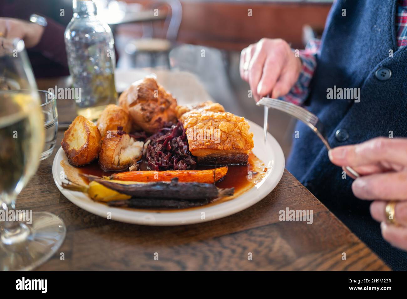 L'épaisse couche d'or crépitant sur le ventre de porc rôti sur une assiette blanche avec des pommes de terre rôties et le Yorkshire pudding avec des légumes dans un restaurant.A ma Banque D'Images