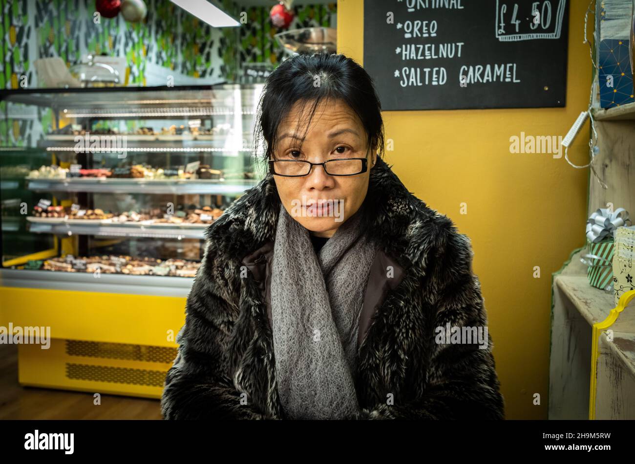 Une femme vietnamienne portant un manteau et un foulard en fausse fourrure est assise dans un café artisanal au chocolat appelé Cenu cacao à King's Parade, Cambridge, Royaume-Uni Banque D'Images