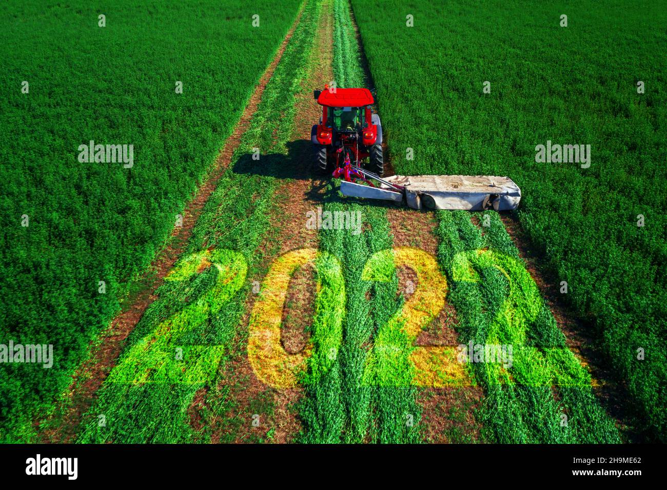 2022 Happy Year concept et tracteur rouge fauchant le champ vert. Banque D'Images