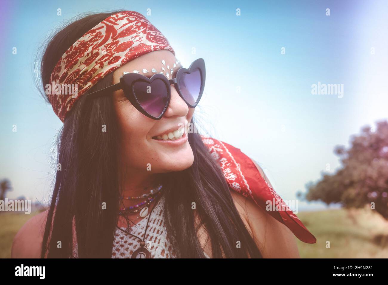 Portrait mat, style rétro d'une femme bohème fraîche, artsy, avec de longs cheveux noirs droits, bandana vintage, bijoux perlés, lunettes de soleil amusantes, paillettes. Banque D'Images