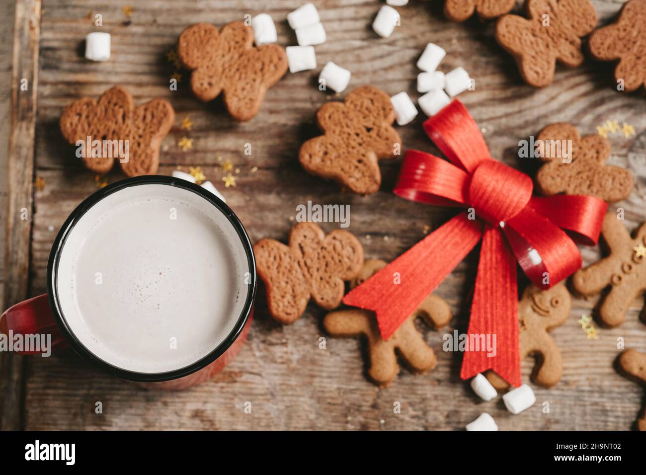 homme de pain d'épice, cacao et biscuits avec un gros noeud rouge sur un fond en bois, vue du dessus.Divers bonbons de noël avec une tasse de cacao sur la table Banque D'Images