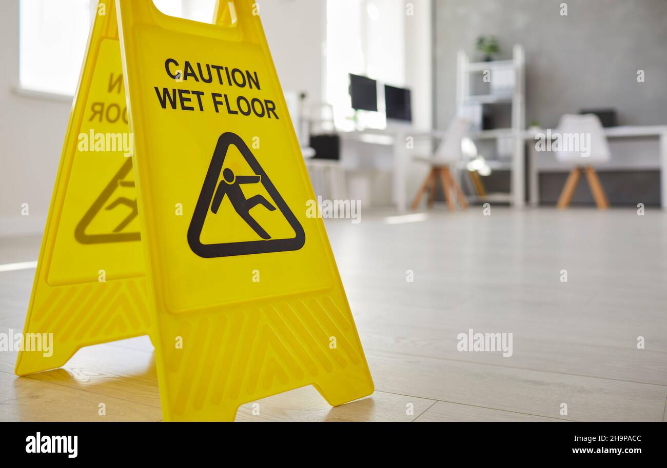 Un gros plan de l'affiche de sécurité en plastique jaune sur pied nous avertit du sol glissant et humide du bureau. Banque D'Images