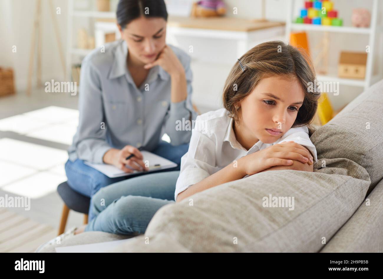 Enfant malheureux assis sur le canapé pendant la séance de thérapie avec un thérapeute ou un psychologue Banque D'Images