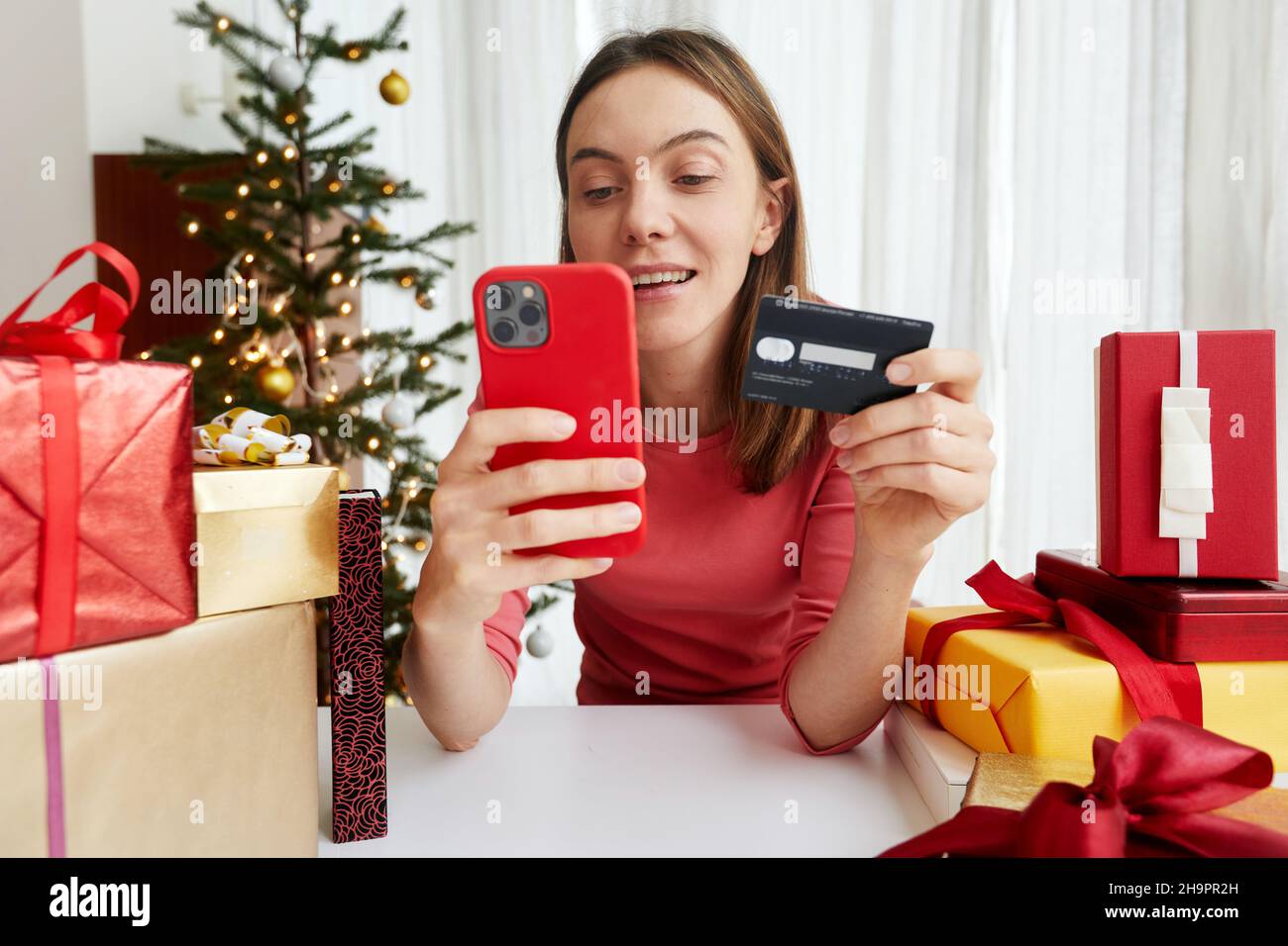 Une femme joyeuse avec carte en plastique shopping en ligne et faire des achats via smartphone tout en achetant des cadeaux de Noël avant les vacances Banque D'Images
