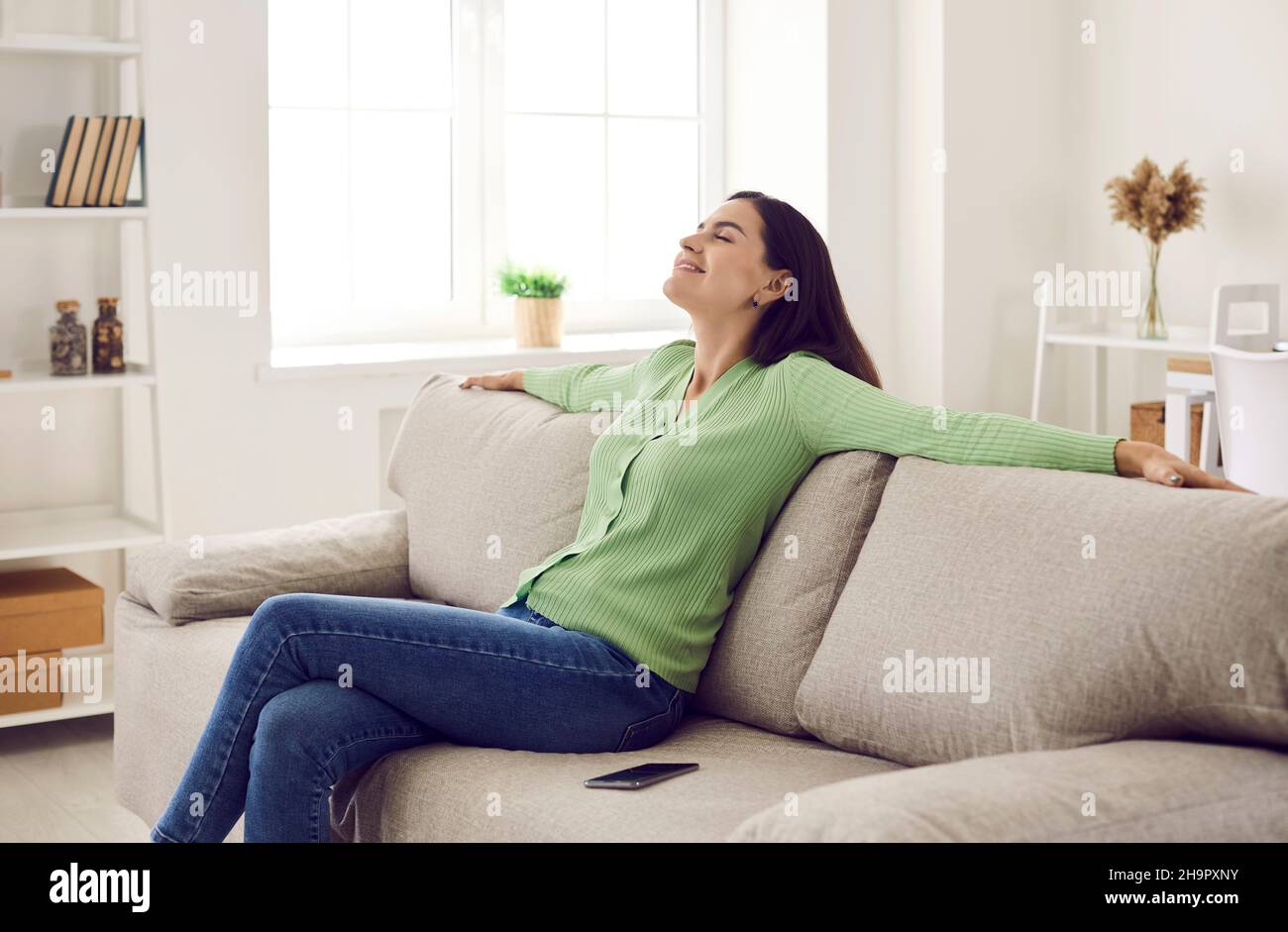 Bonne jeune femme se relaxant sur un canapé confortable dans le salon de son propre appartement Banque D'Images