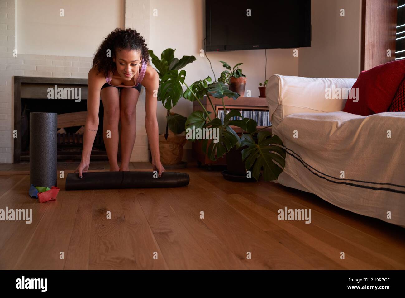 Happy Multi-culture jeune femme adulte roulant tapis de yoga dans le salon moderne à la maison Banque D'Images