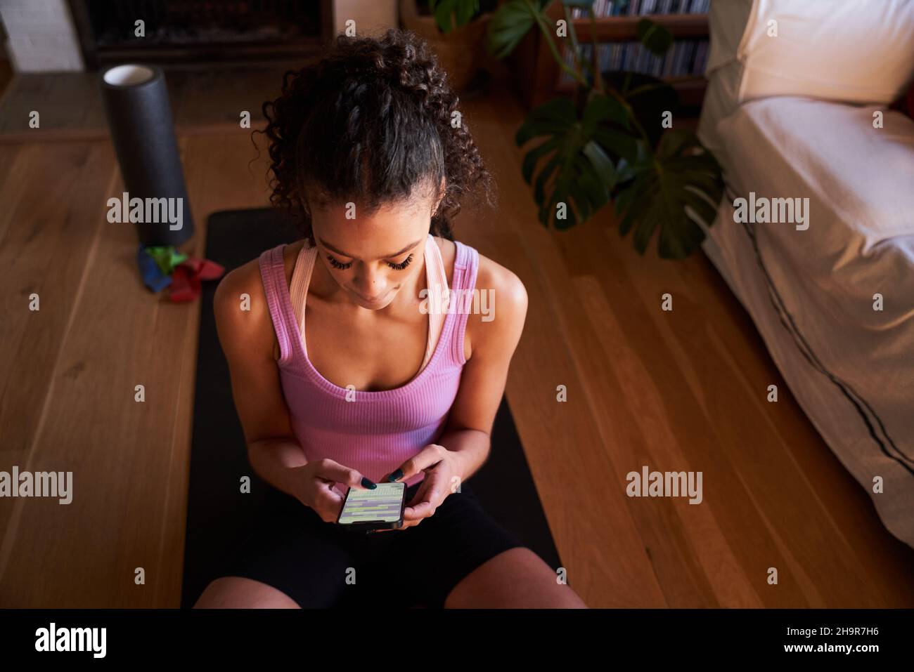 Happy Multi-culture jeune femme adulte textant sur tapis de yoga dans le salon moderne à la maison Banque D'Images