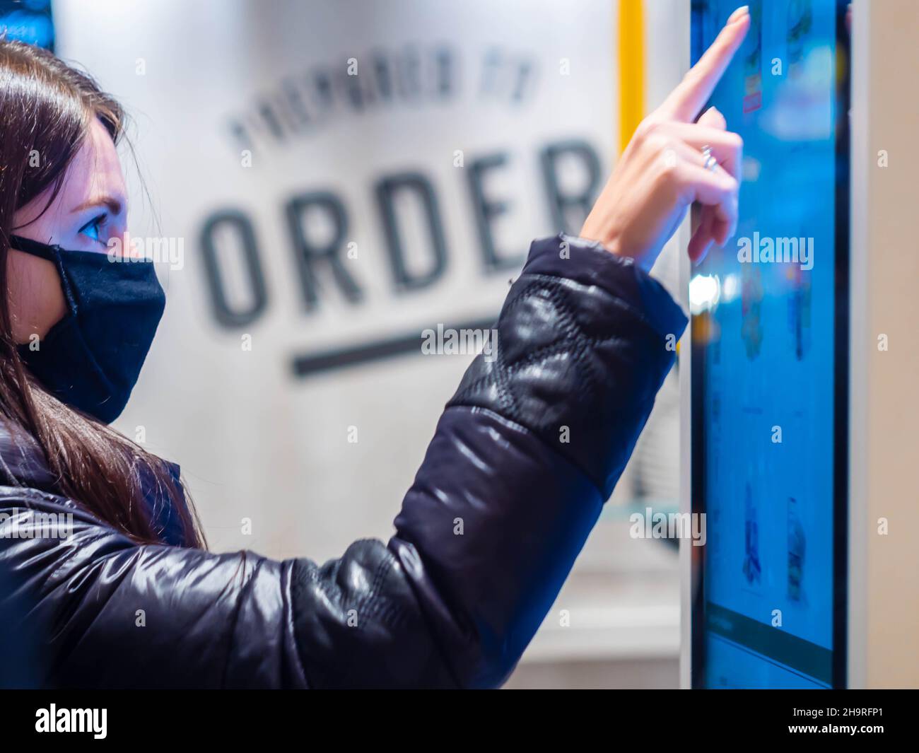 Moscou, Russie -3 avril 2021: Une jolie fille caucasienne dans un masque achète une boisson chaude chez McDonald's.Machines de commande en libre-service à l'intérieur de McDonald's. Banque D'Images