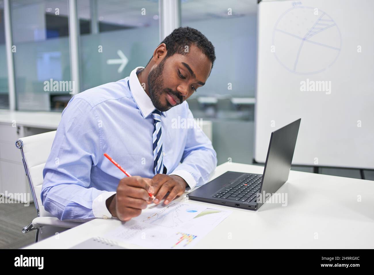 Homme d'affaires africain travaillant sur un ordinateur portable tout en analysant des données au bureau Banque D'Images