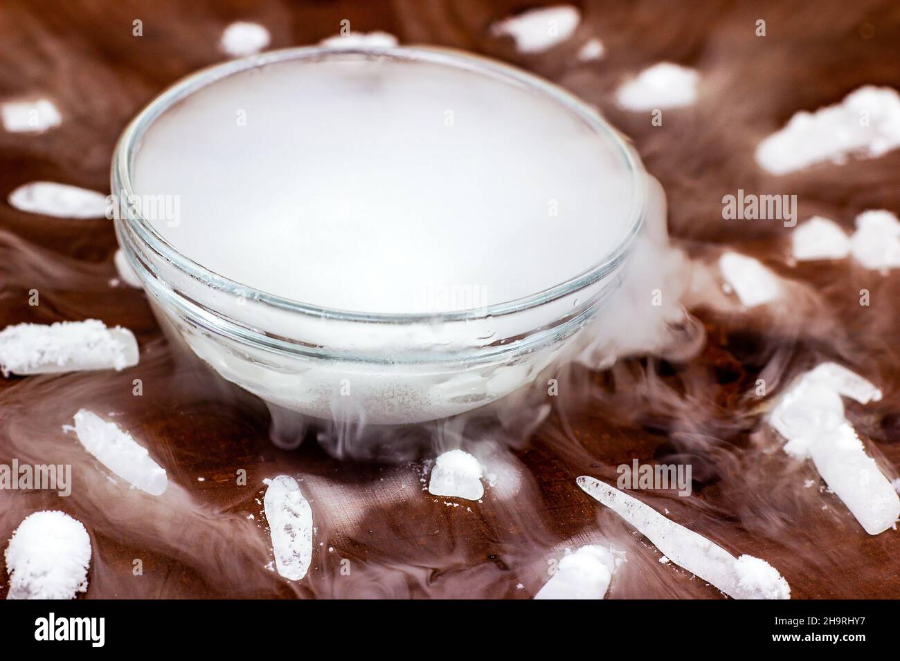 Glace sèche froide blanche (dioxyde de carbone gelé) avec effet de fumée dans le bol en verre sur fond de bois brun foncé. Banque D'Images