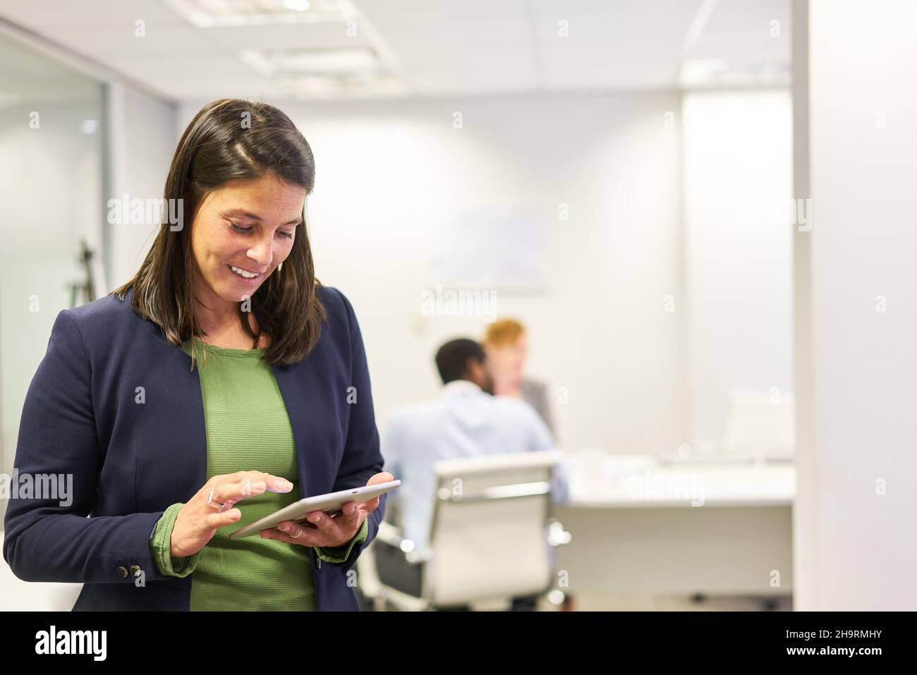 Femme d'affaires souriante effectuant des recherches sur les tablettes électroniques en ligne au bureau Banque D'Images