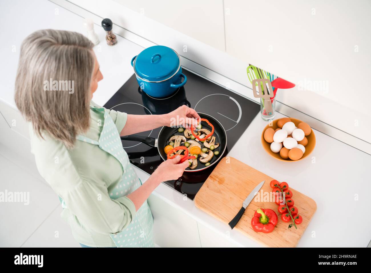 Haut au-dessus de la vue en grand angle portrait d'une femme à cheveux gris attrayante faisant de la cuisine maison recette de repas friture ingrédients à la maison blanc clair intérieur Banque D'Images
