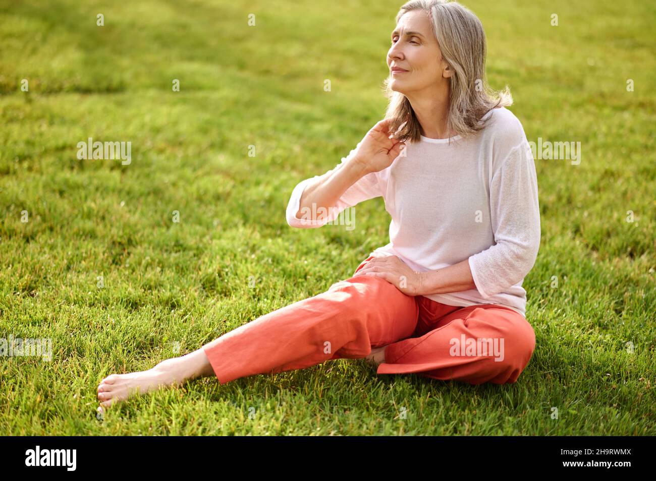 Femme assise sur l'herbe regardant pensivement à côté Banque D'Images