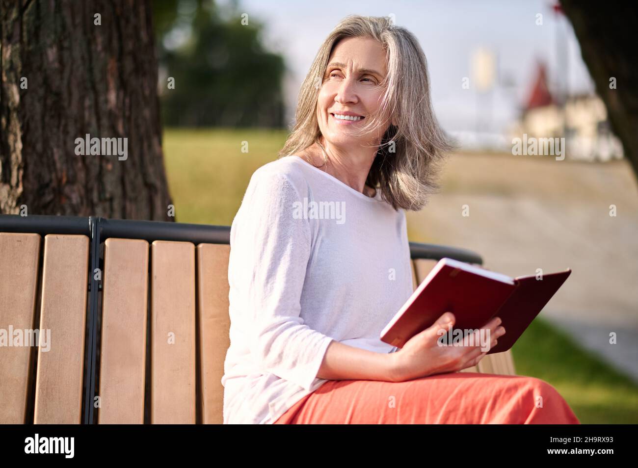 Femme avec livre assis dans le parc regardant à côté Banque D'Images