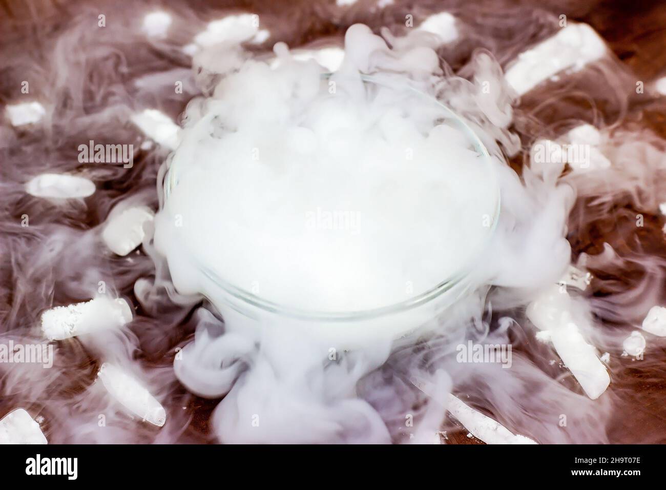 Glace sèche froide blanche (dioxyde de carbone gelé) avec effet de fumée dans le bol en verre sur fond de bois brun foncé. Banque D'Images
