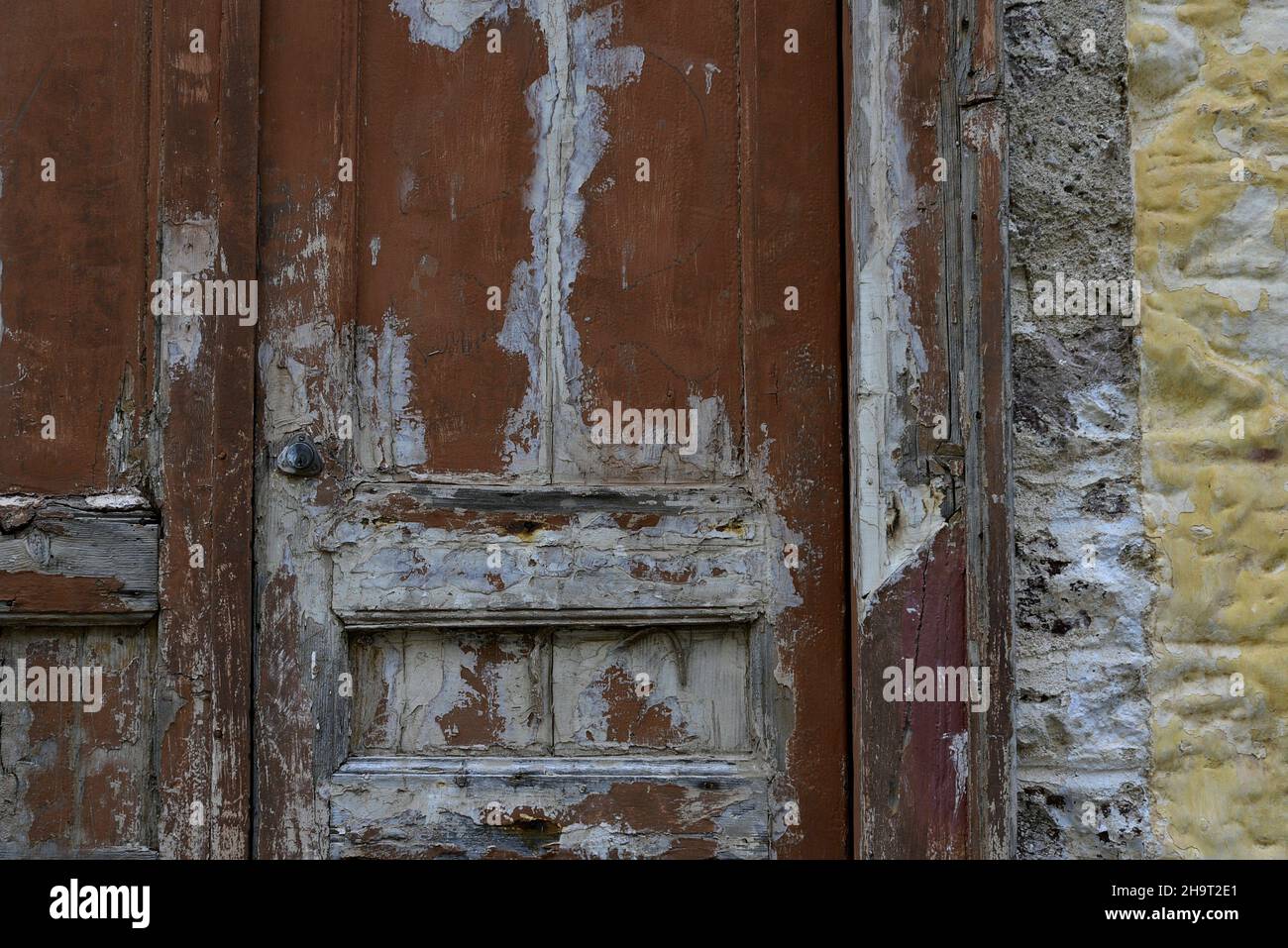 Ancienne porte en bois décolorée contre un mur de pierre ocre abîmé à Nafplio, Grèce. Banque D'Images