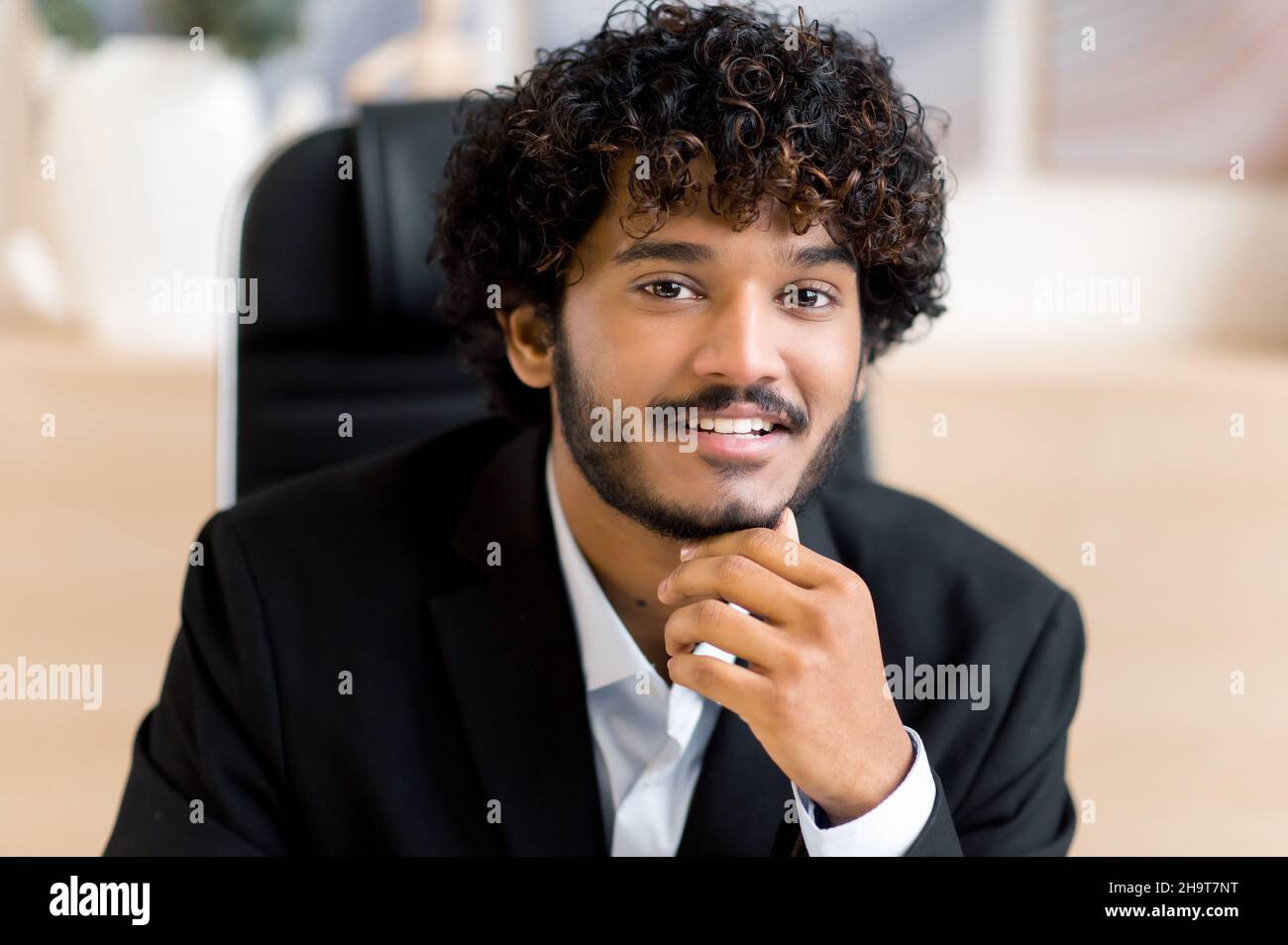 Portrait d'entreprise en gros plan.Sympathique souriant homme d'affaires indien aux cheveux bouclés, propriétaire de petite entreprise, chef d'entreprise ou directeur des ventes, en costume formel, agent immobilier réussi, regardant la caméra Banque D'Images