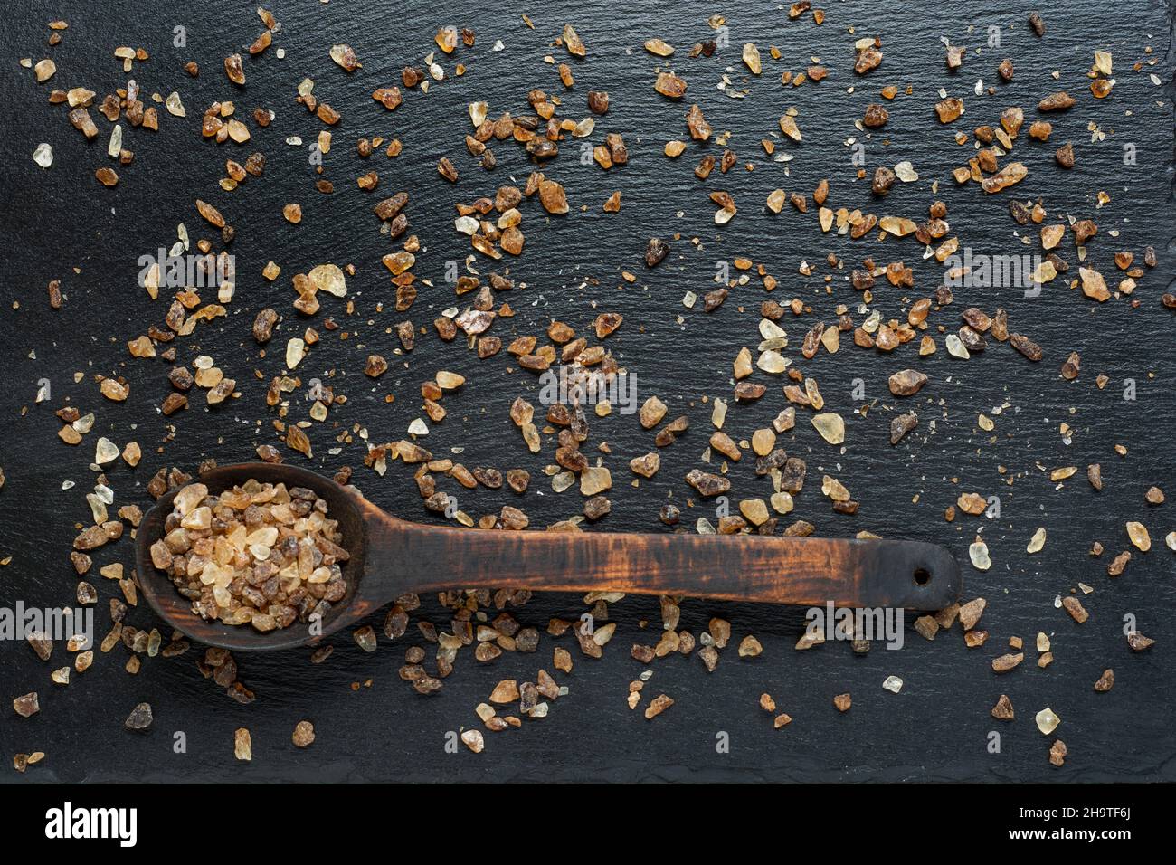 Cuillère en bois pleine de sucre granulé brun foncé sur fond d'ardoise gros plan. Banque D'Images