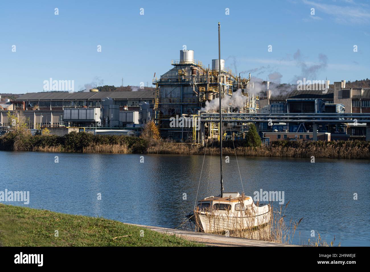 Un petit bateau-pilote amarré dans un canal avec des structures industrielles en arrière-plan Banque D'Images