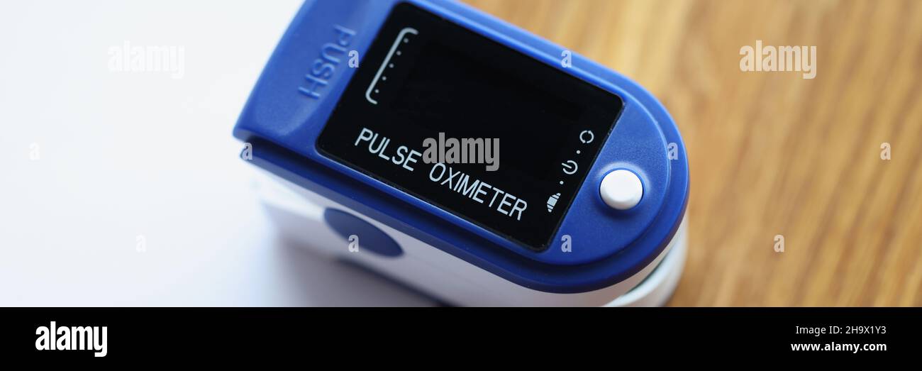 Oxymètre de pouls bleu posé sur une table en bois avec des documents à proximité Banque D'Images