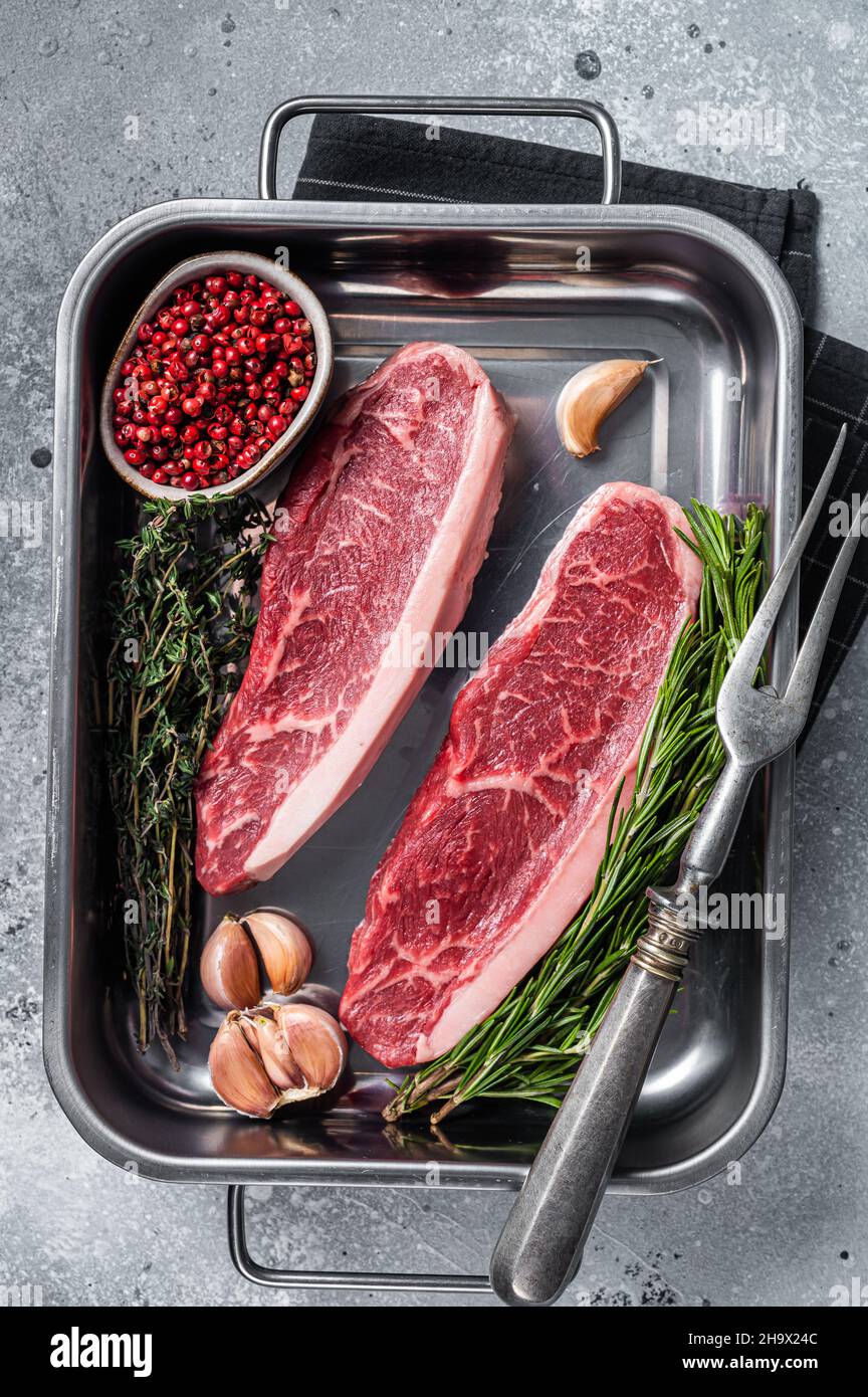 Bœuf de bœuf haché cru ou steak de bœuf de bœuf haché dans le plateau avec des herbes.Arrière-plan gris.Vue de dessus Banque D'Images