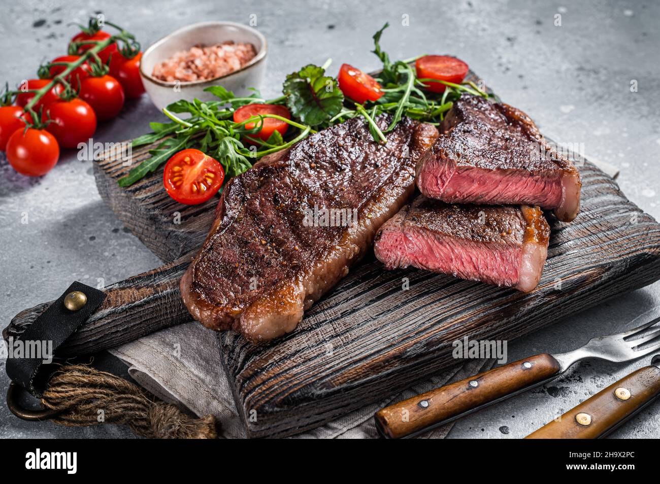 Steak de viande de bœuf rôti au chapeau ou au sirloin supérieur sur une planche de bois avec salade.Arrière-plan gris.Vue de dessus Banque D'Images