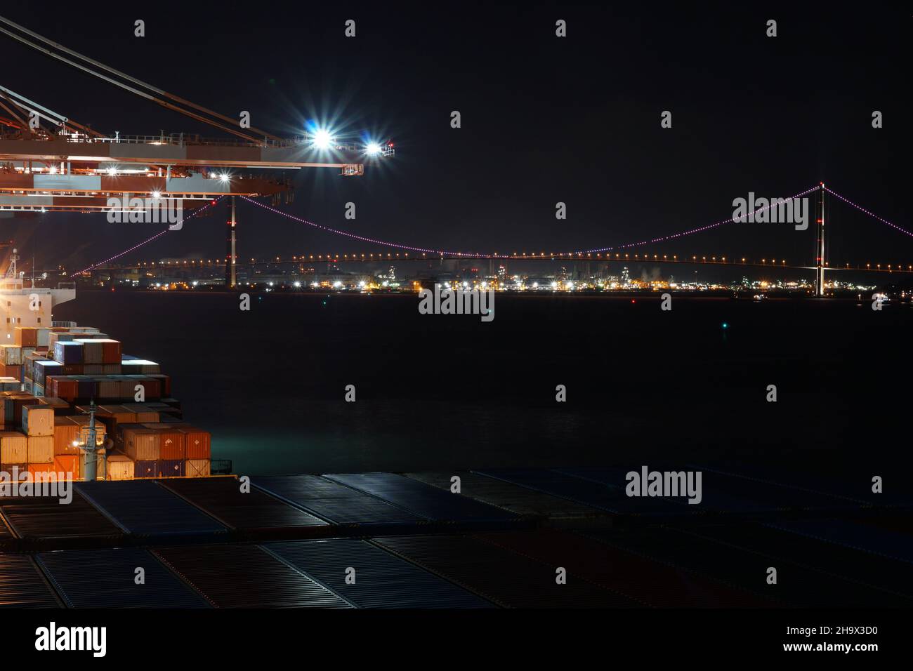 Vue de nuit depuis le terminal à conteneurs avec grues portiques et navires dans le port sur le pont Yi Sun-Sin à suspension lumineuse. Banque D'Images