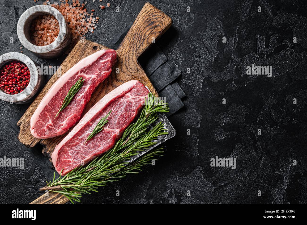 Steak de viande de bœuf de boucherie ou sirloin sur le dessus du butcher.Arrière-plan noir.Vue de dessus.Copier l'espace Banque D'Images