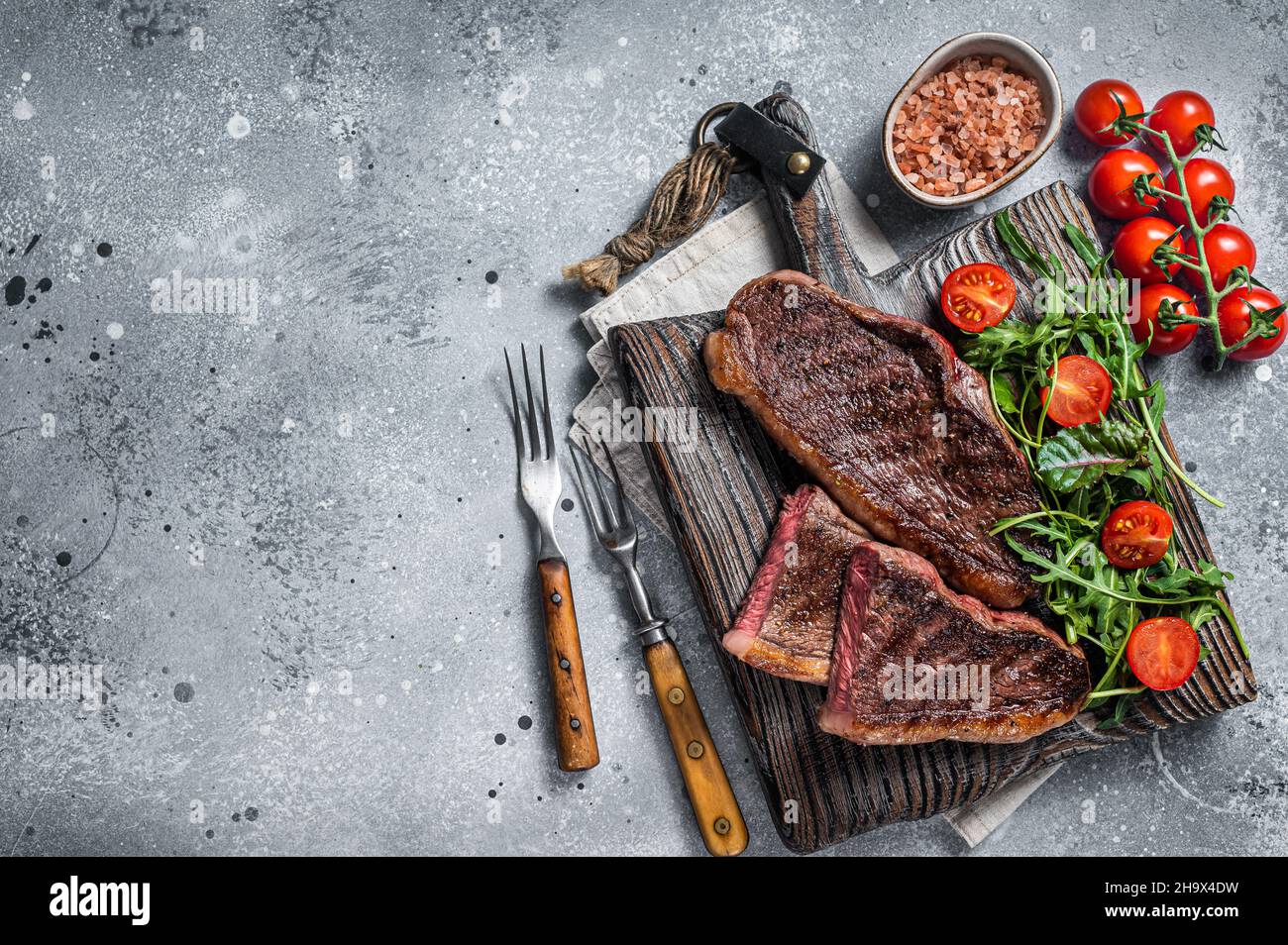 Steak de viande de bœuf rôti au chapeau ou au sirloin supérieur sur une planche de bois avec salade.Arrière-plan gris.Vue de dessus.Copier l'espace Banque D'Images