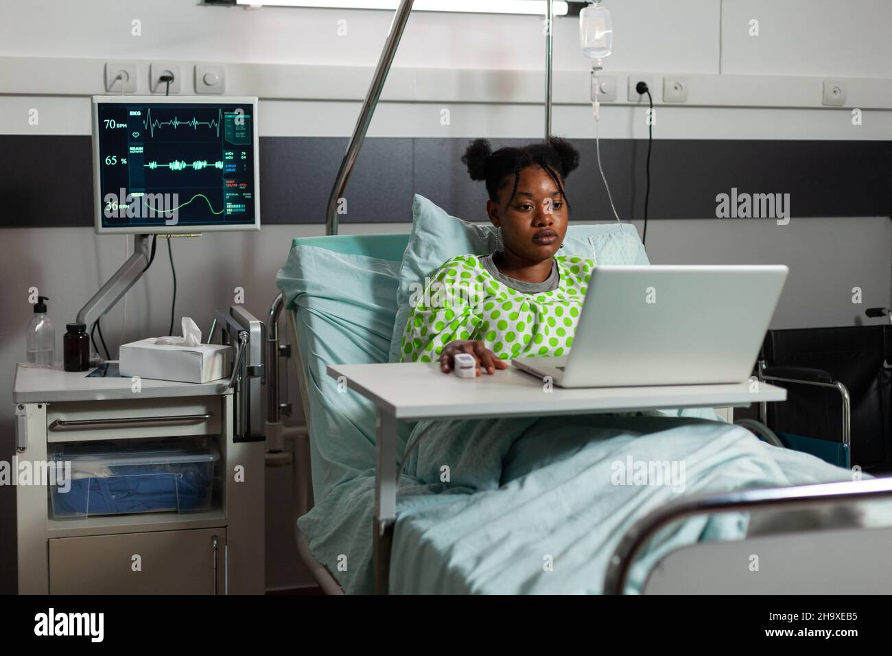 Malade afro-américain debout au lit pendant un rendez-vous médical regardant des vidéos amusantes en ligne sur ordinateur portable.Jeune femme se rétablissant après une chirurgie dans la salle d'hôpital.Services de médecine Banque D'Images