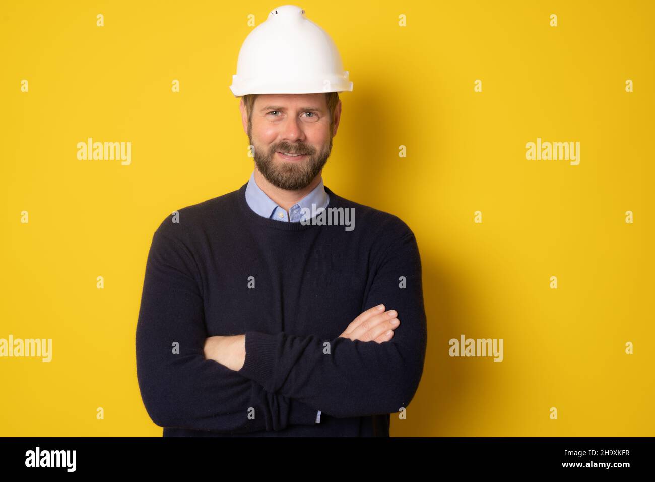 Jeune architecte homme portant un casque d'entrepreneur avec les bras repliés sur un fond jaune isolé Banque D'Images