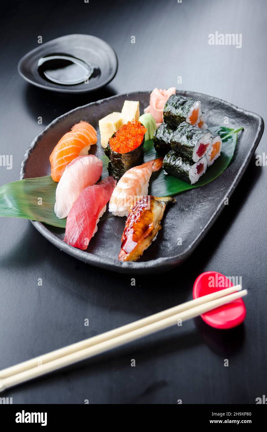 Assiette de sushis japonais frais mélangés avec saumon, thon, yellowtail, nigiri de crevettes, maki de saumon,maki de thon sur une assiette noire et une table noire Banque D'Images