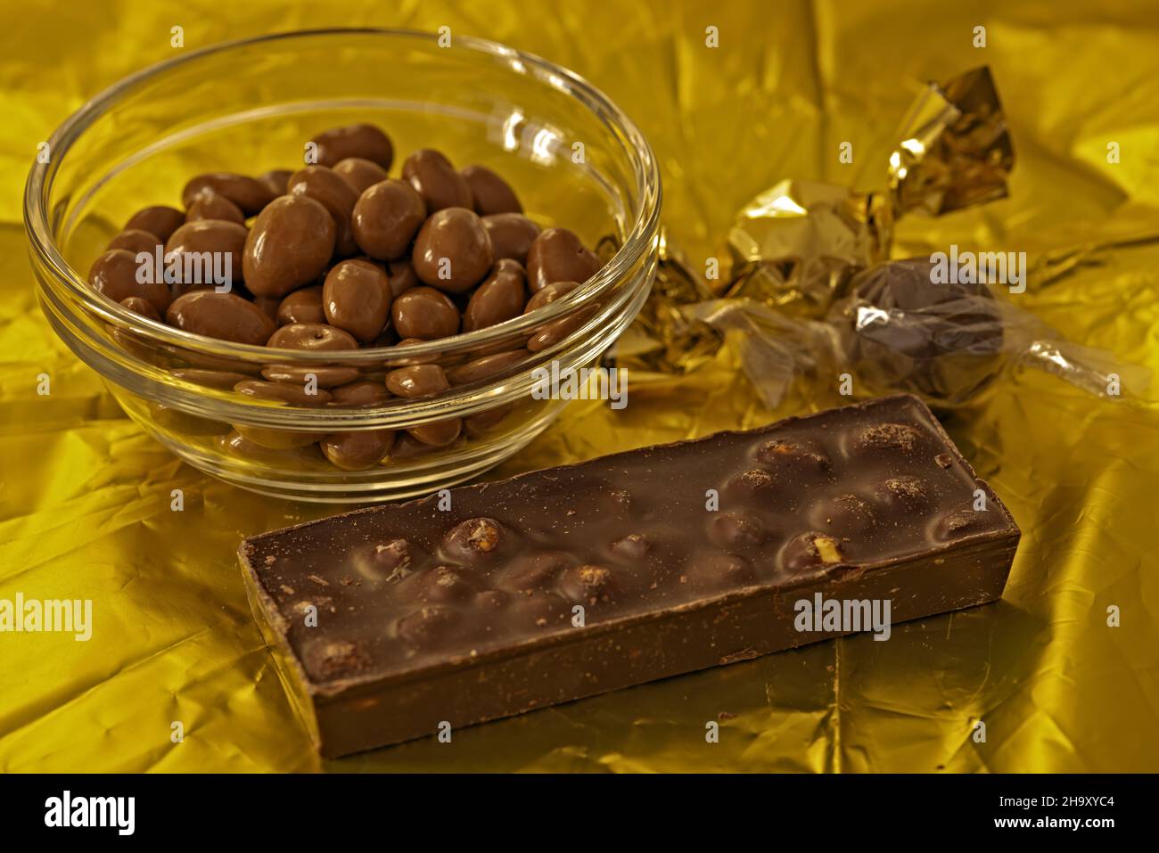 arachidi ricoperte al gianduia nella ciotola di vetro su fondo dorato con pezzo di cioccolato alle nocciole vista da sopra Banque D'Images