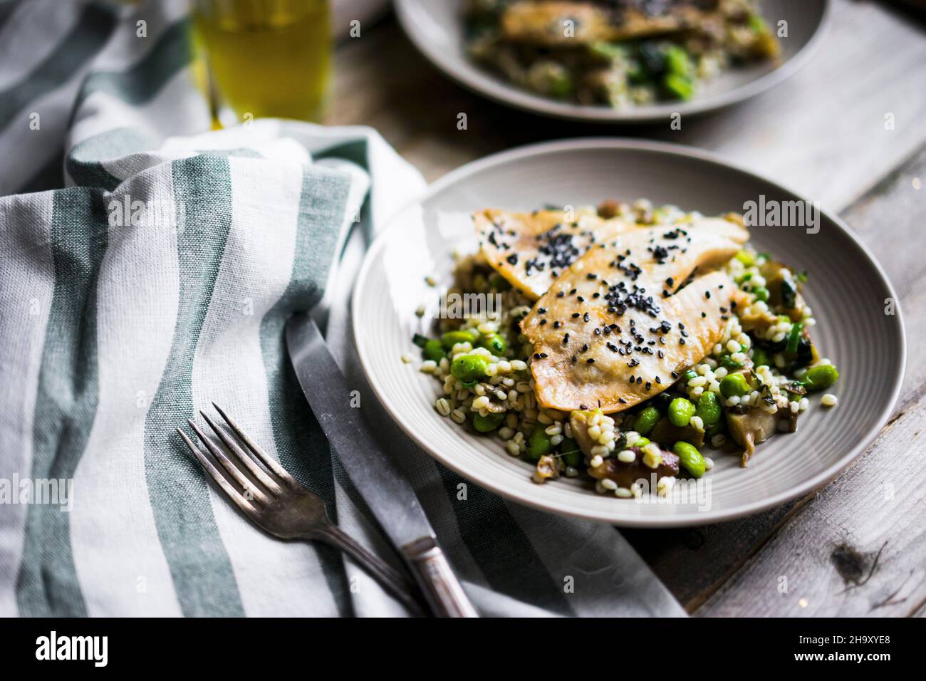 Filet de poisson grillé avec risotto aux champignons et haricots édamames sur une surface rustique Banque D'Images