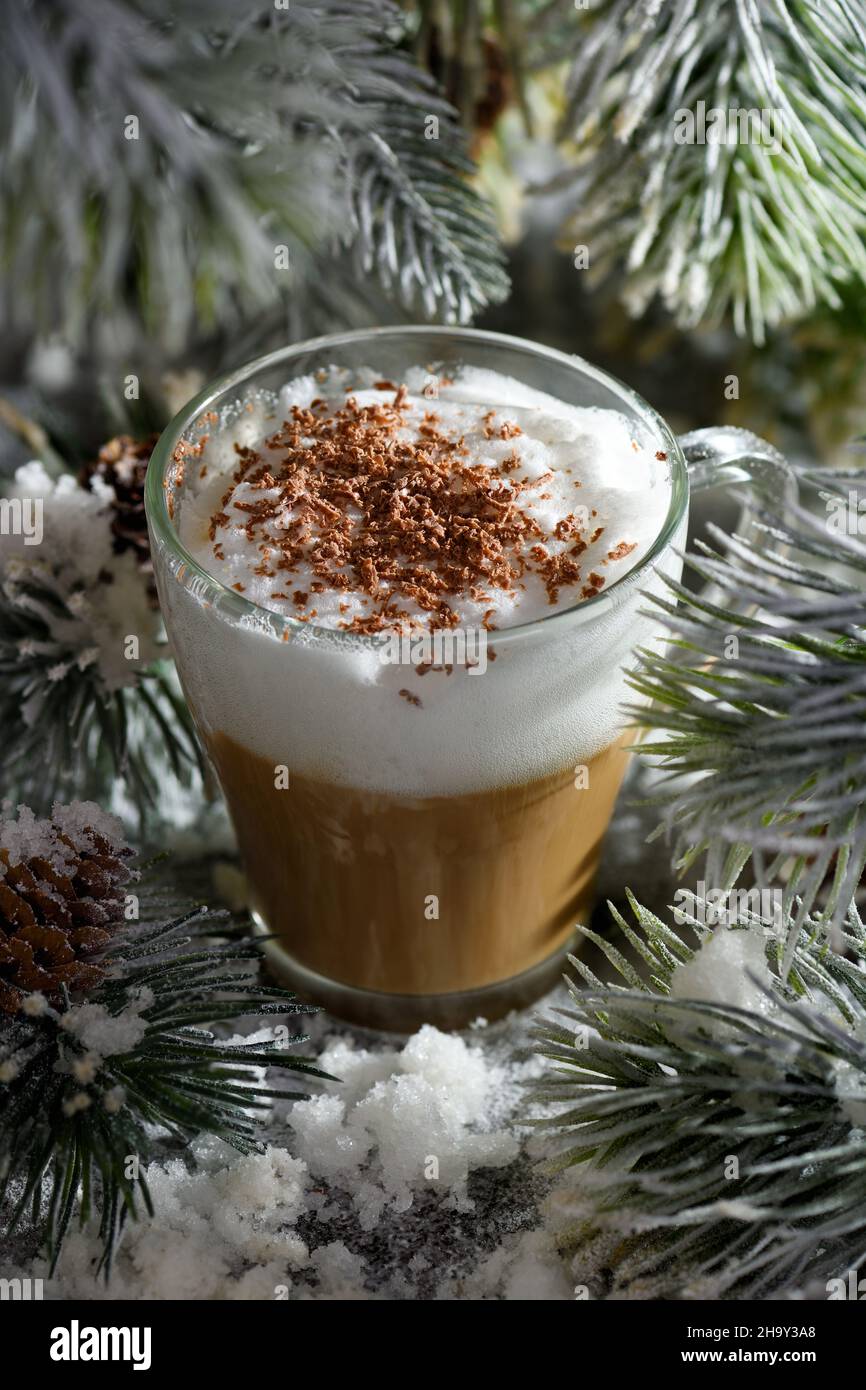 Latte macchiato de Noël. Une grande boisson chaude au café avec des copeaux de chocolat, parmi les branches de pin enneigées et la neige. Banque D'Images