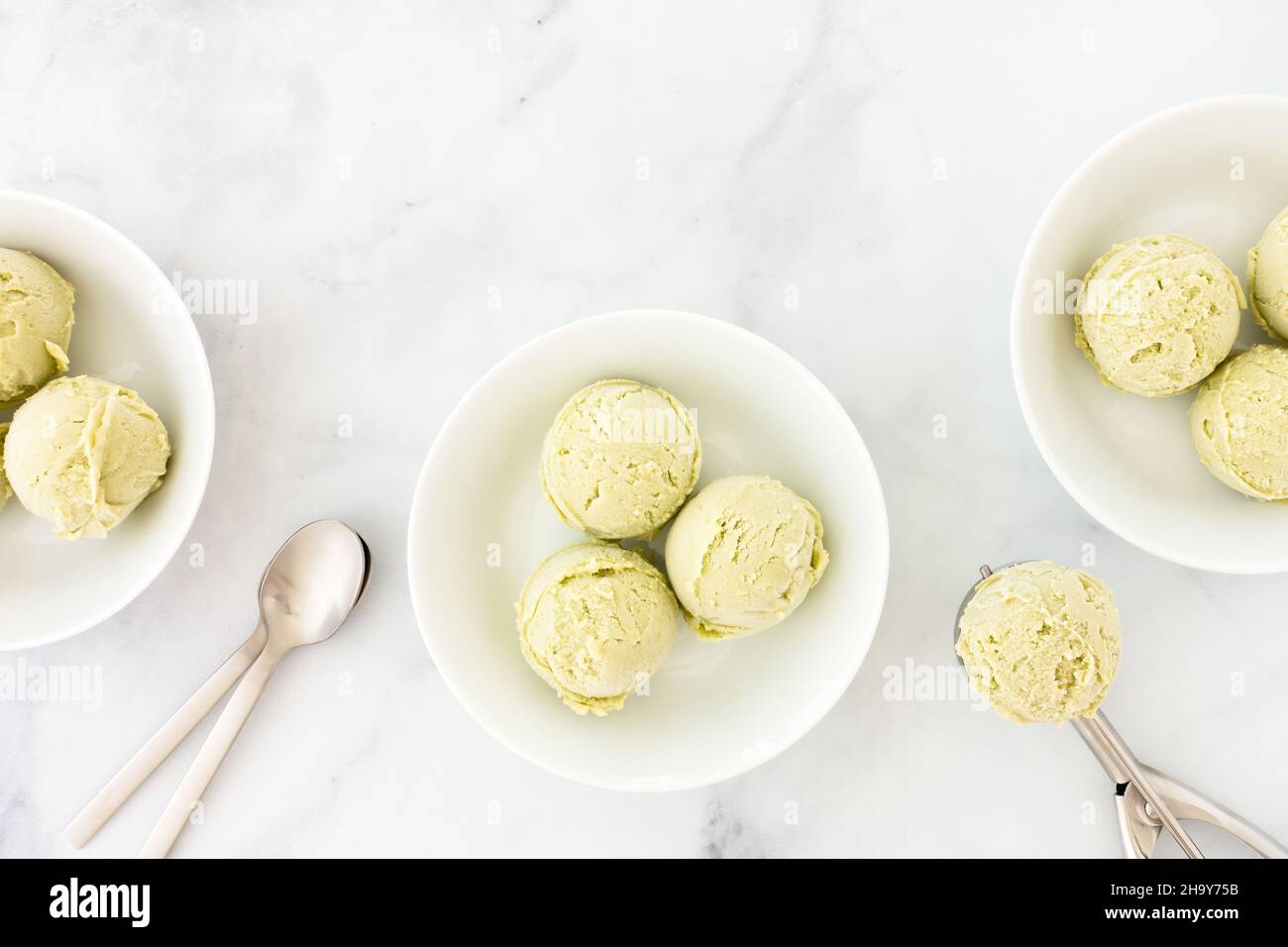 Des boules de crème glacée à l'avocat maison dans des bols blancs et sur une cuillère de crème glacée au-dessus du marbre blanc avec espace pour les copies.Vue de dessus. Banque D'Images
