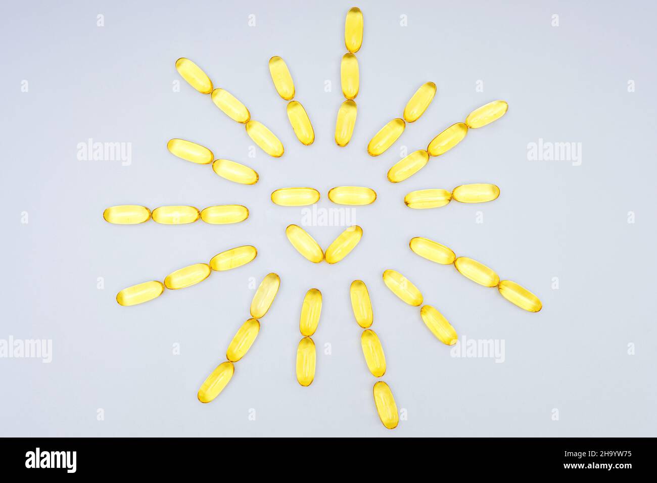 Capsules de gel souple à l'huile de poisson disposées en forme de soleil, isolées sur un fond neutre.Supplément alimentaire en vitamine D. Banque D'Images
