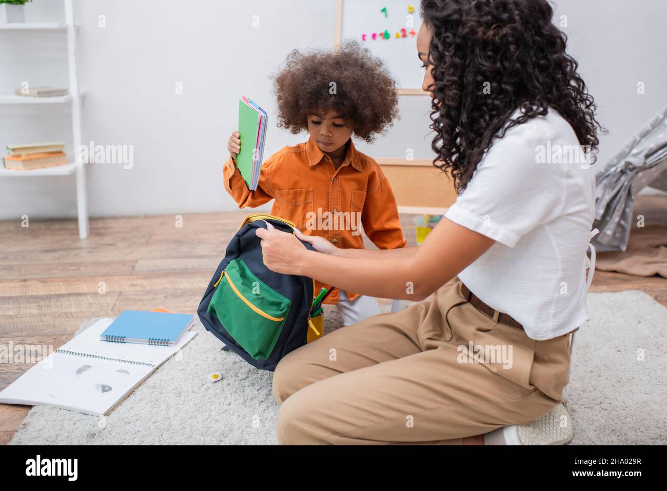 Enfant afro-américain tenant le carnet près de la mère avec sac à dos dans la salle de séjour Banque D'Images