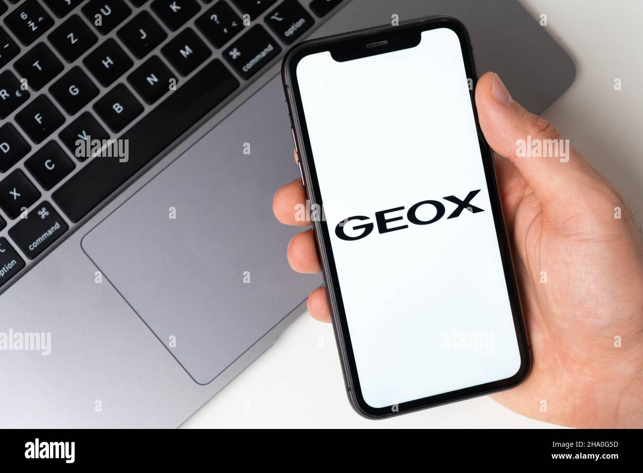 Logo de l'application Geox sur l'écran de l'iPhone pour faire des achats en ligne avec un ordinateur portable en arrière-plan.Novembre 2021, San Francisco, États-Unis Banque D'Images