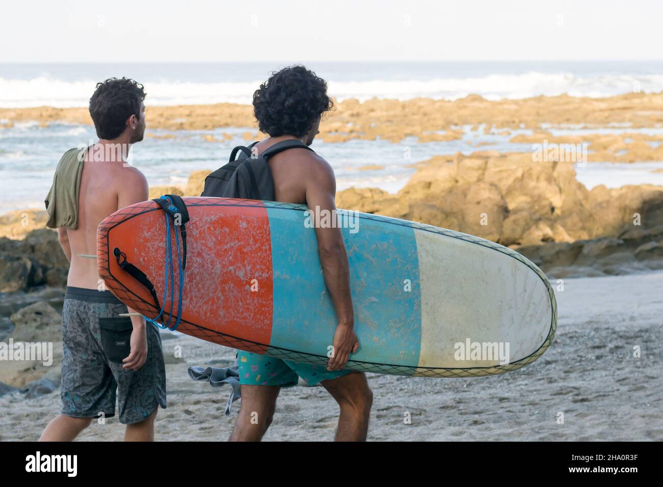 Vue arrière des hommes qui portent une planche de surf tout en marchant sur la plage Banque D'Images