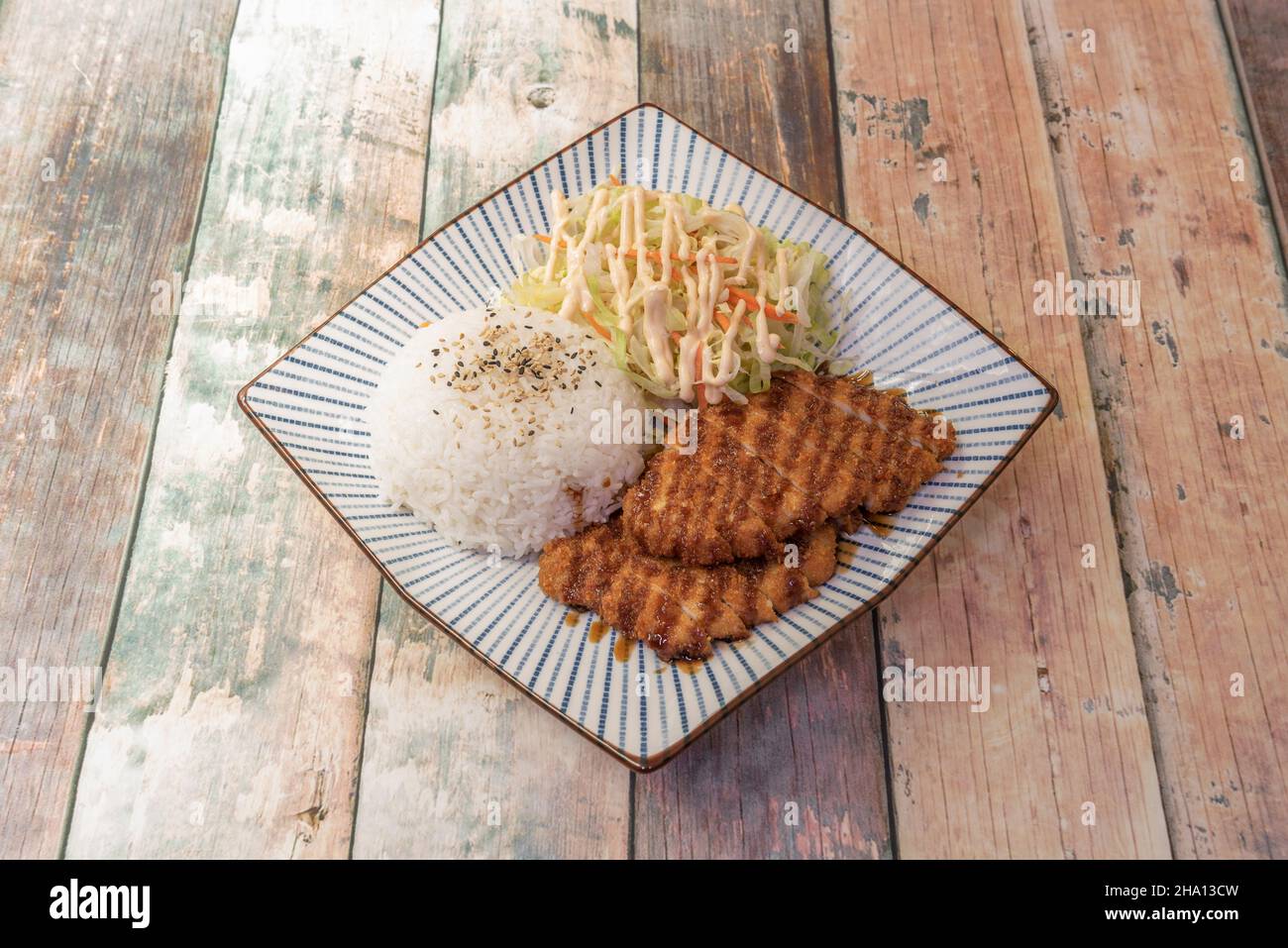 Receta asiática de solomillo de cerdo crujiente con salsa yakitori, ensalada de verduras y arroz blanco con semillas de sésamo y amapola en un platon d Banque D'Images