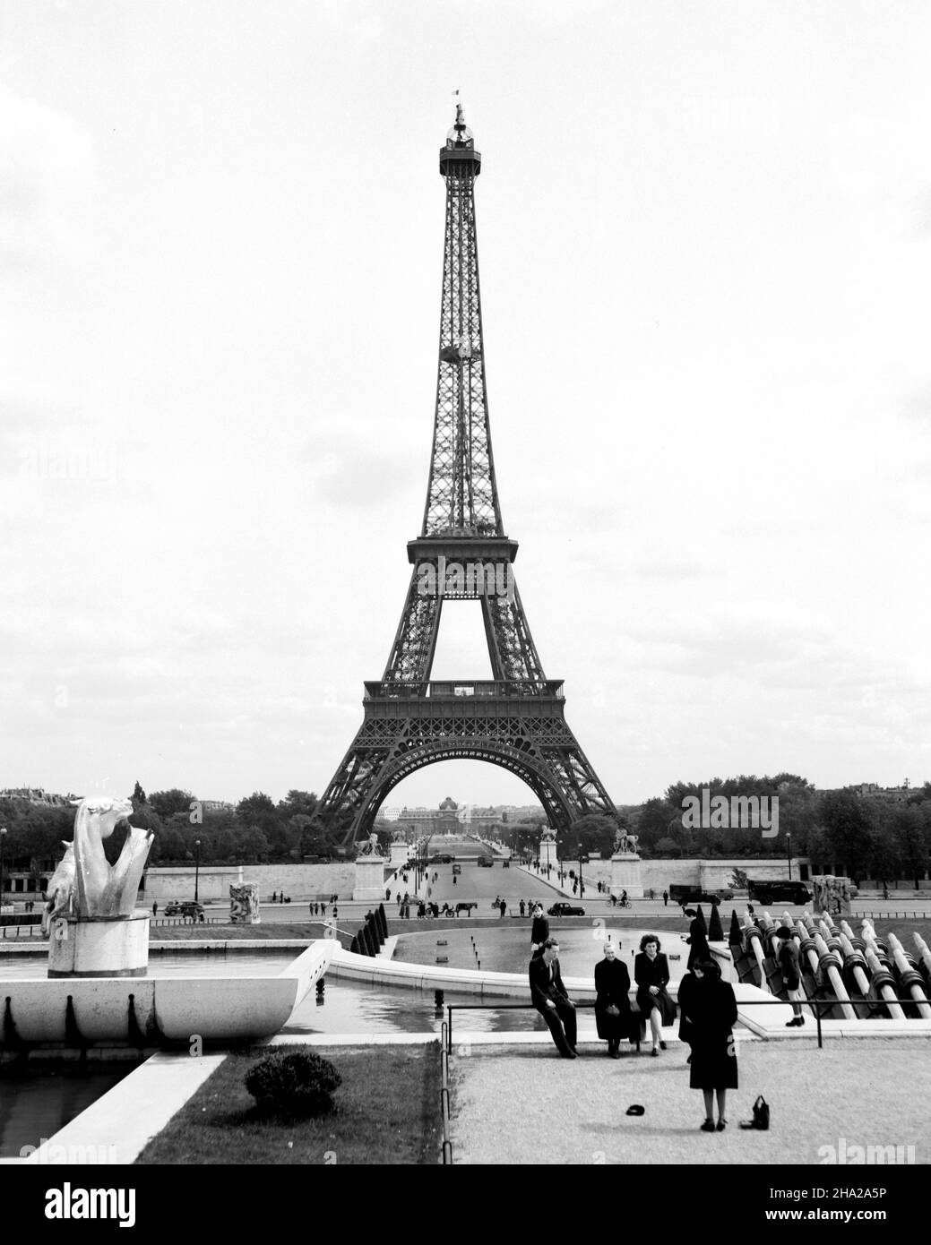 Paris Tour Eiffel 1945 depuis les jardins du Trocadéro.Vue en hauteur de la tour prise du dessus de la fontaine des Jardins du Trocadéro (Jardins du Trocadéro) la position de la caméra est légèrement au-dessus et peut-être à 20 pieds d'une famille de huit.Une femme en robe semble arranger une photo d'une partie de la famille avec la tour en arrière-plan.Le groupe familial au premier plan semble avoir de 5 à 80 ans.Au-dessous d'eux, il y a beaucoup de gens à pied à la base de la fontaine et se promène sur le pont d'lena. Banque D'Images