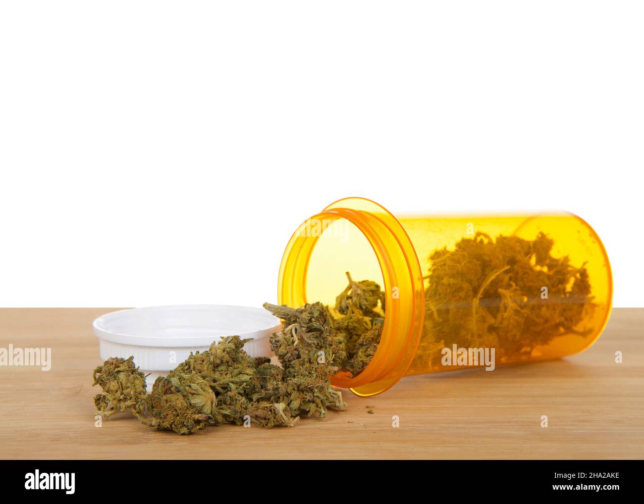 Bouteille de prescription avec des bourgeons de cannabis qui se répandent sur une table en bois clair, couvercle à bouteille derrière le produit.Isolé sur blanc. Banque D'Images