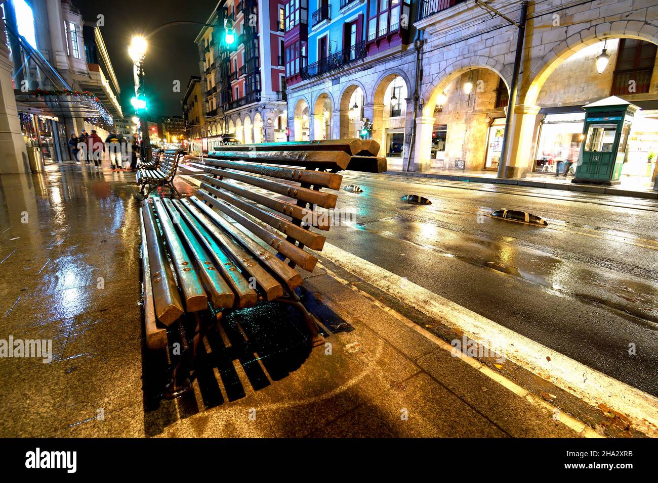 Banc en bois mouillé à la tombée de la nuit avec pluie devant les arcades de Ribera à Bilbao Banque D'Images