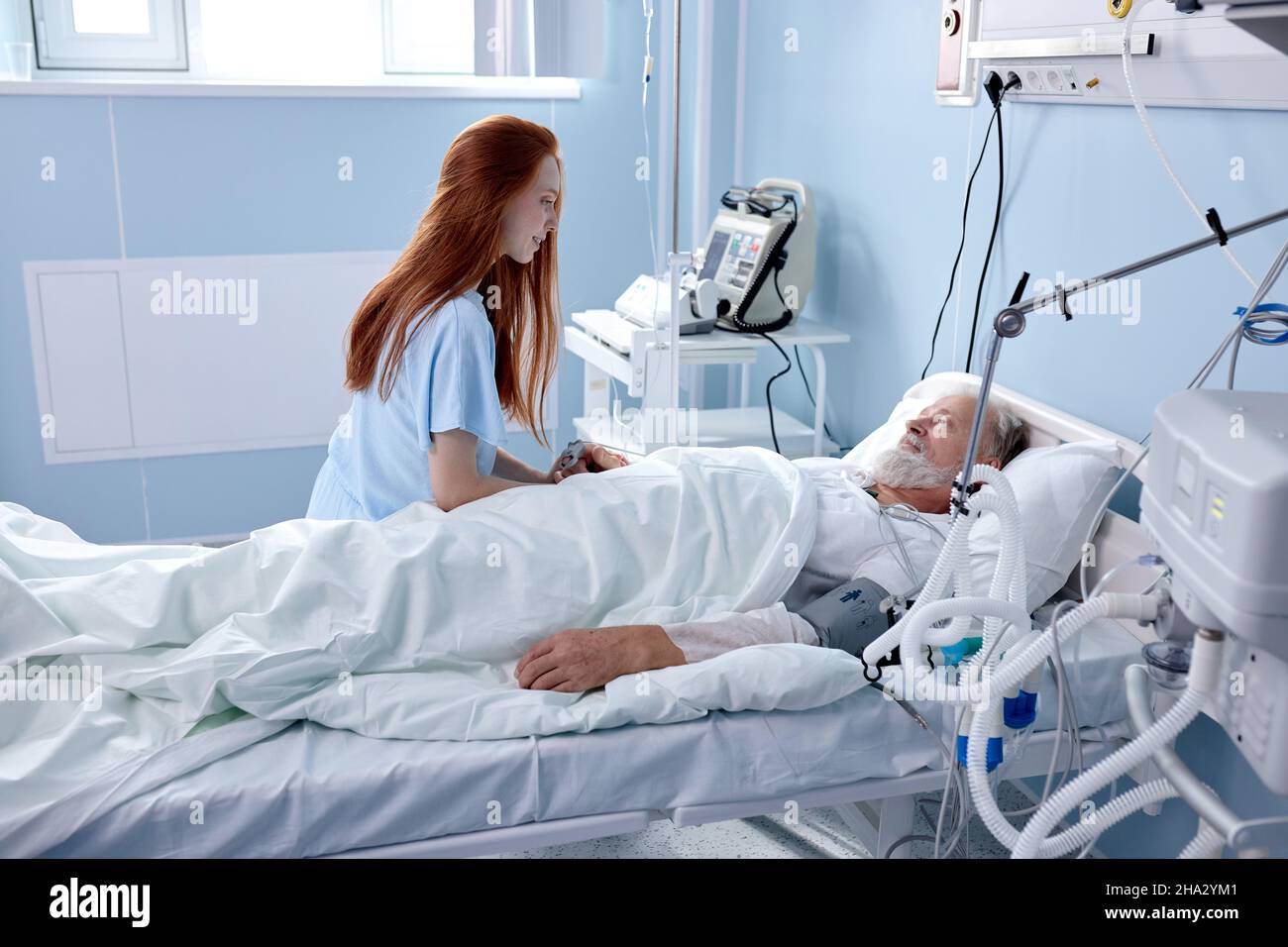 une adorable femme caucasienne est venue rendre visite à un père ou à un grand-père, qui est couché dans une salle d'hôpital moderne pendant le coronavirus ou l'épidémie de covid-19. redhead Banque D'Images